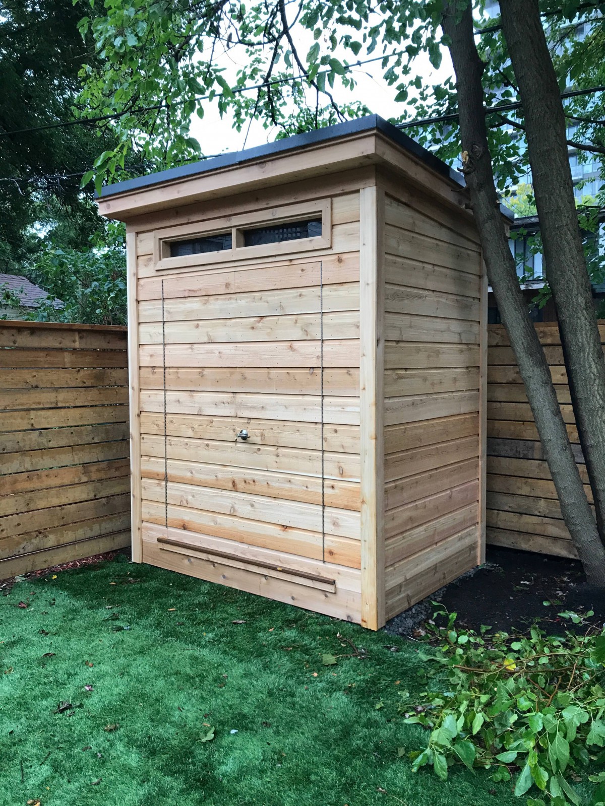 Cedar Dune shed design 5' x 7' in a backyard featuring with concealed wooden double doors and a transom window as seen from the side. Id number 242476-2. jpeg.