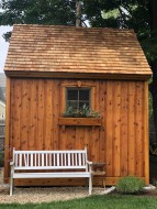 Cedar telluride shed design 10' x 10' in a backyard featuring antique door style as seen from the front. Id number 5746.
