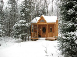Canmore small cabin plan 14 x 14 with a single screen door in a yard seen from the front. ID number 3384-2.