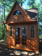 Bala Bunkie cabin design with a fan arch window and a shed dormer in woods seen from the front. ID number